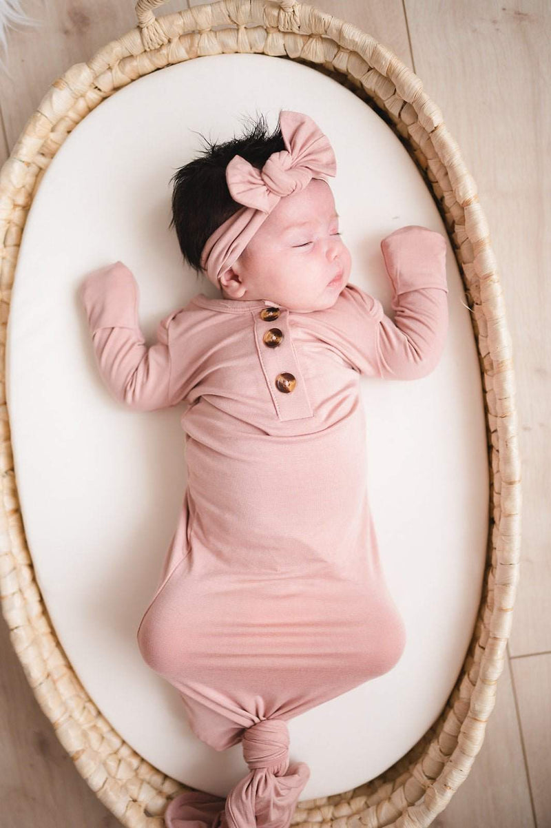 Dusty pink bamboo knotted baby gown with fold-over cuffs in a woven basket.