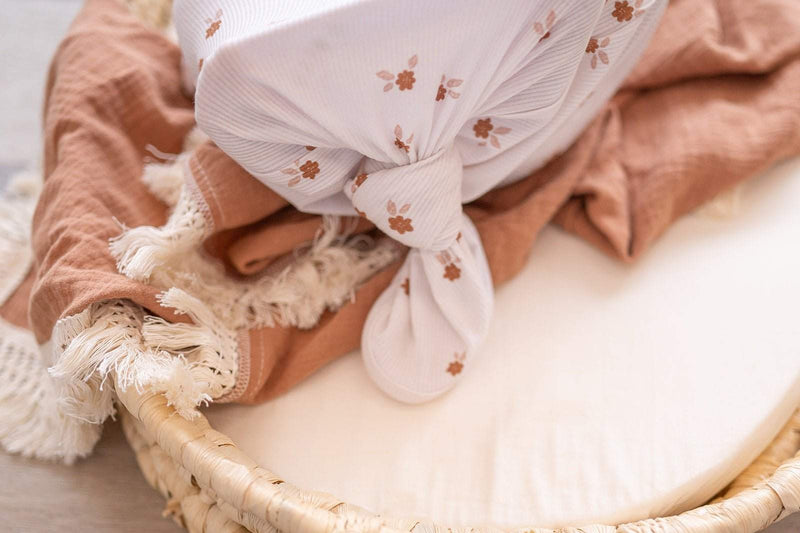 Knotted baby gown with floral pattern in bamboo viscose material on a brown and white blanket.