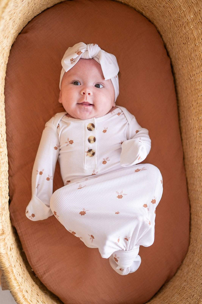 Knotted baby gown in floral design with button details and fold-over cuffs on an infant in a cozy setting.