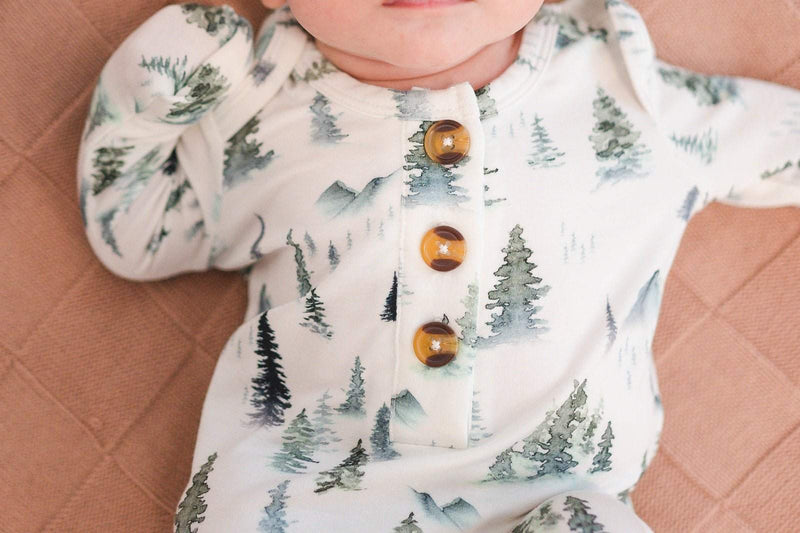 Green forest knotted baby gown with buttons and tree pattern, gender-neutral design.