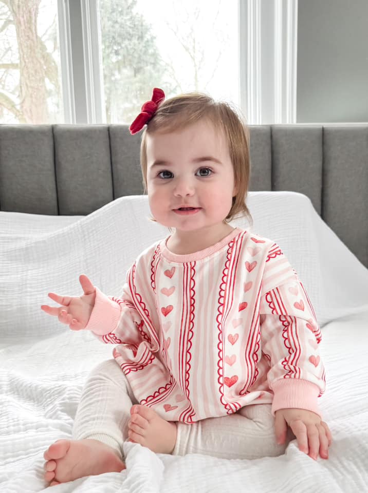 Baby wearing Laced with Love organic cotton sweatshirt romper with lace trim detail, smiling.