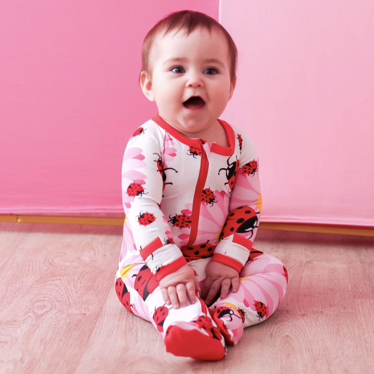 Baby footie pajamas in a red and pink ladybug print with covered feet and a full-length front zipper.