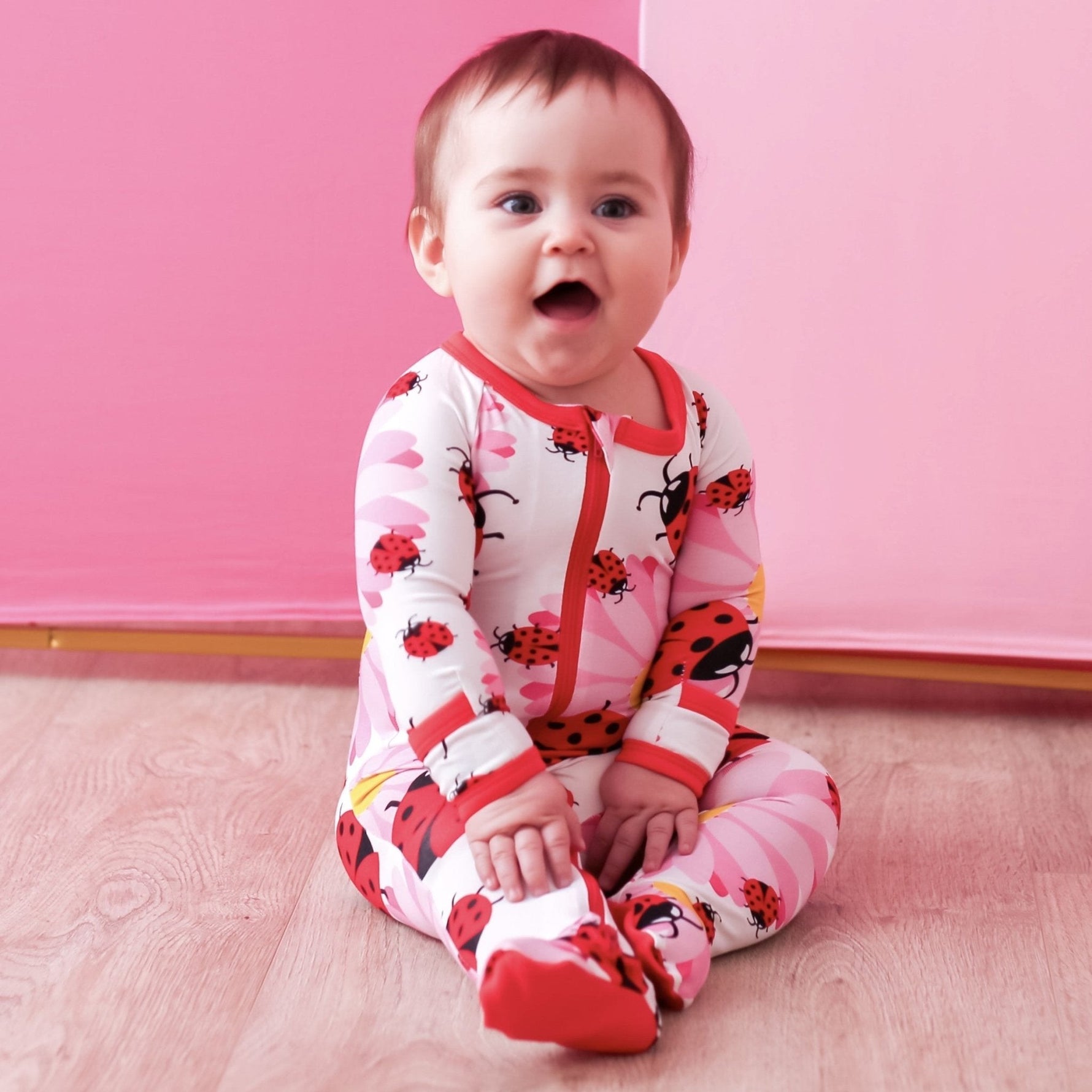Baby footie pajamas in a red and pink ladybug print with covered feet and a full-length front zipper.