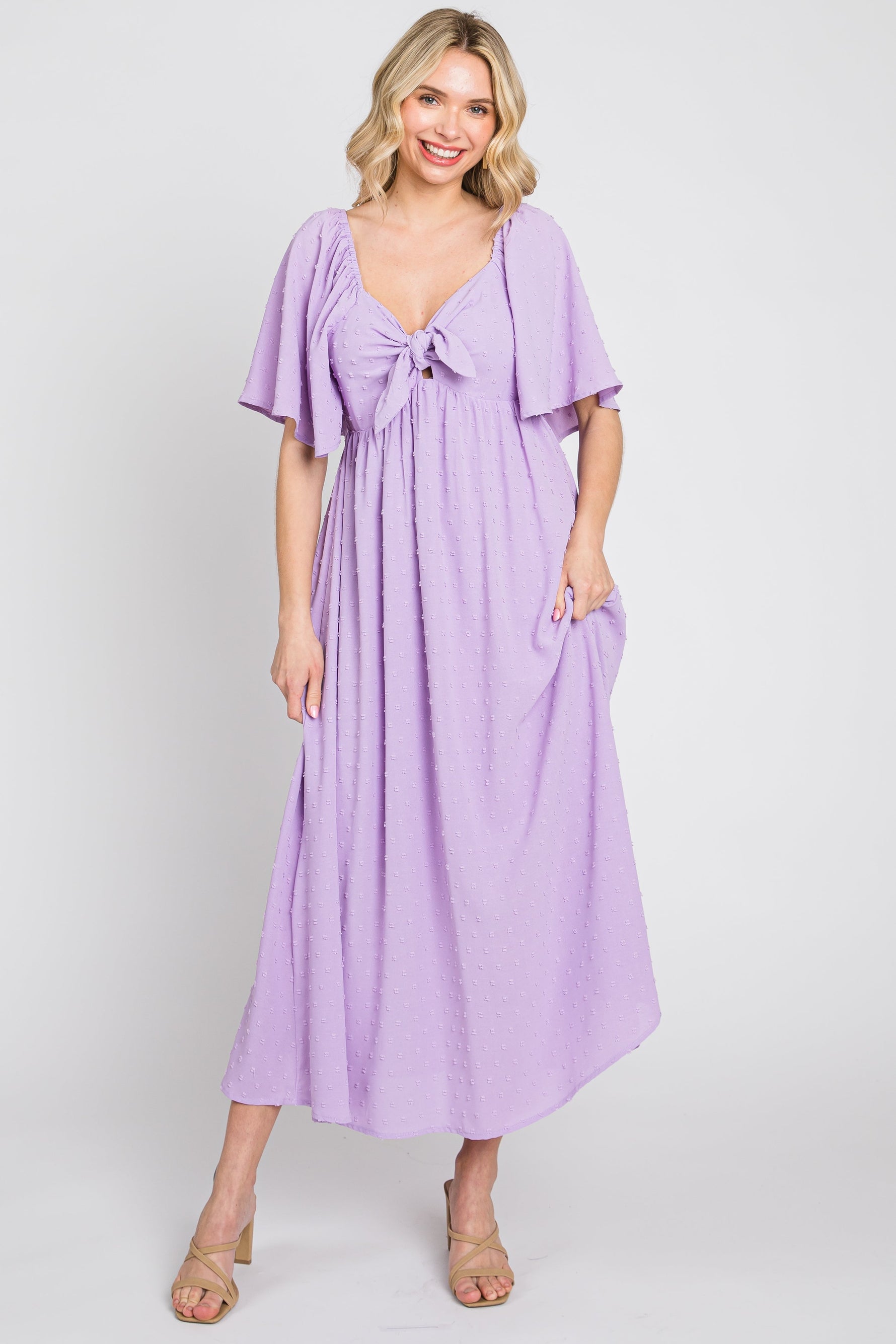 Baby girl wearing a lavender textured dot midi dress with front tie and ruffle sleeves.