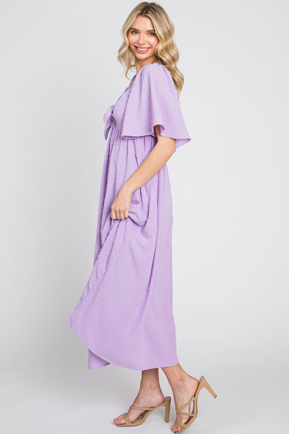 Baby girl wearing a lavender textured dot midi dress with front tie and ruffle sleeves.