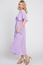 Baby girl wearing a lavender textured dot midi dress with front tie and ruffle sleeves.