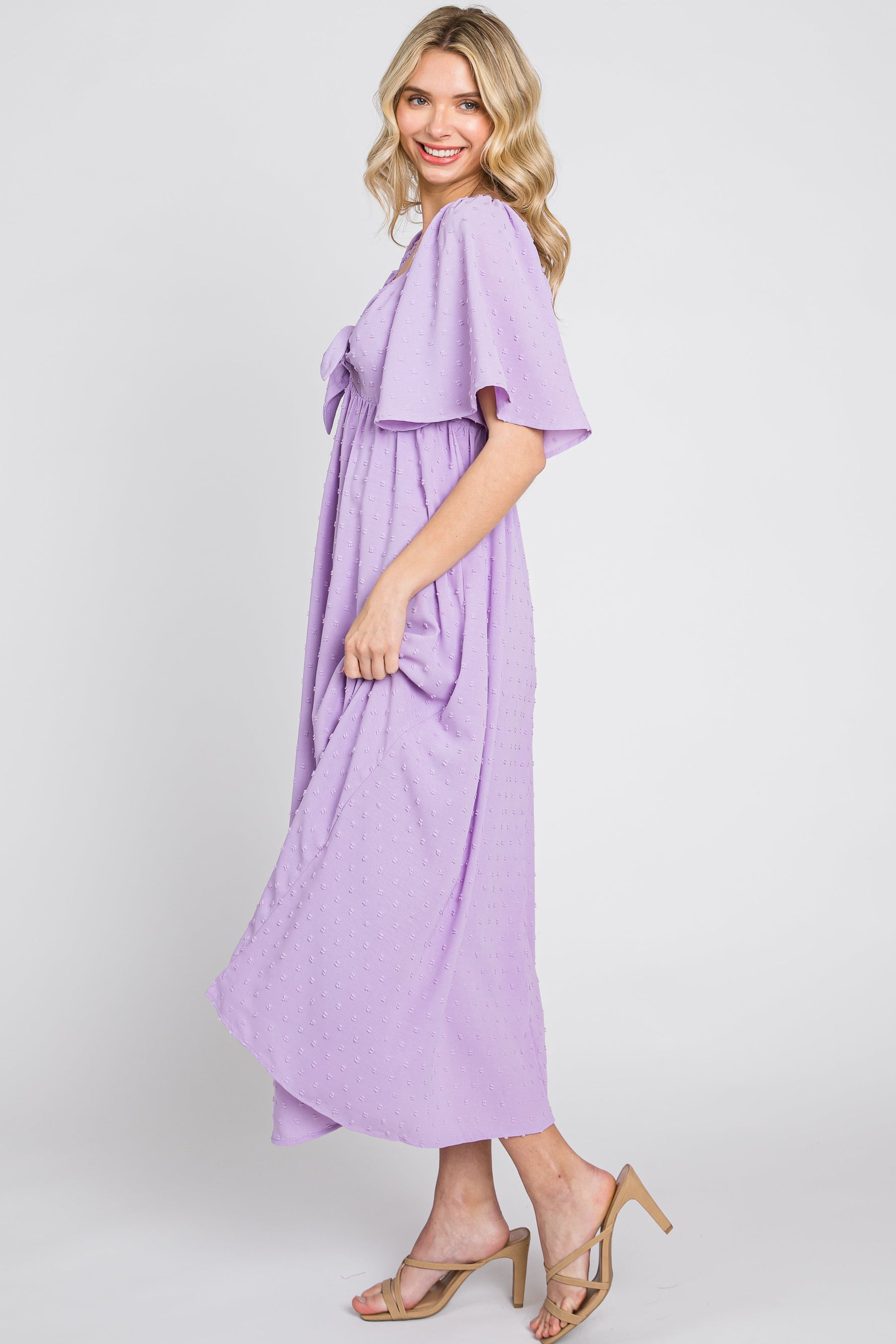 Baby girl wearing a lavender textured dot midi dress with front tie and ruffle sleeves.