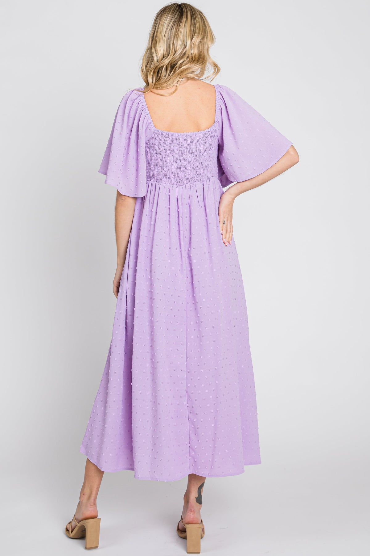 Baby girl wearing a lavender textured dot midi dress with front tie and ruffle sleeves.