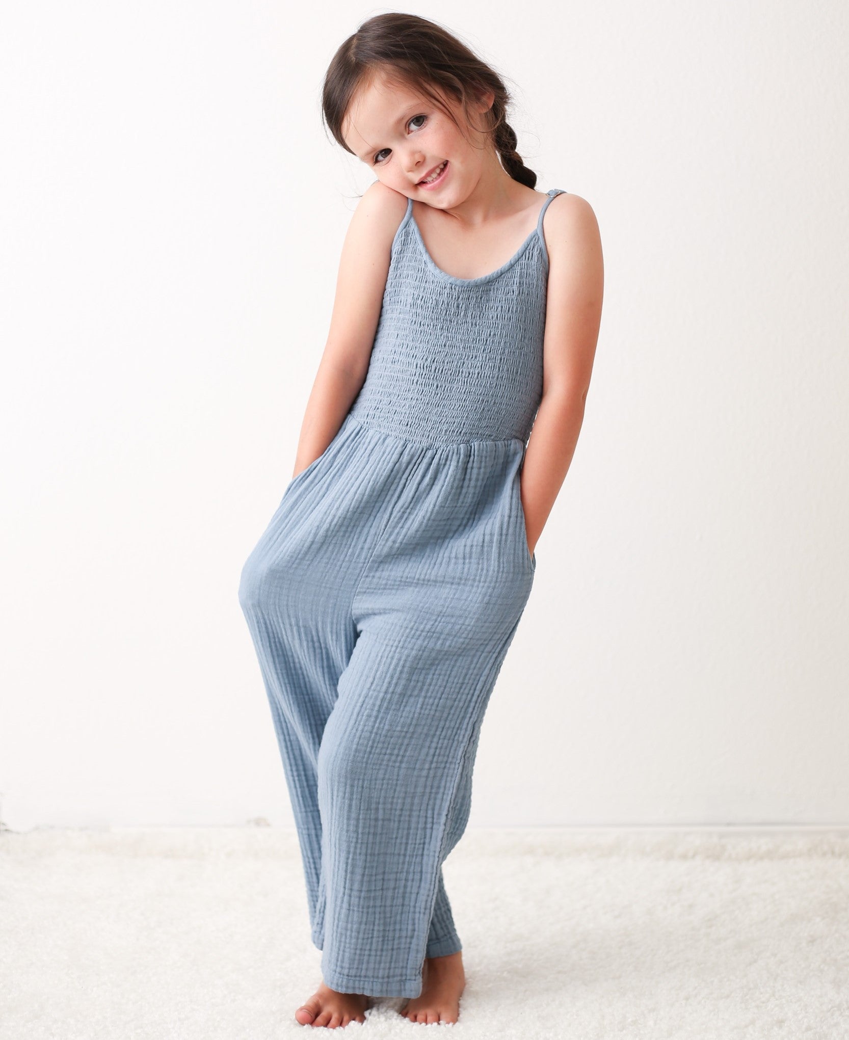 Skye blue baby jumpsuit in gauze fabric with smocked top, pocket, and adjustable straps.