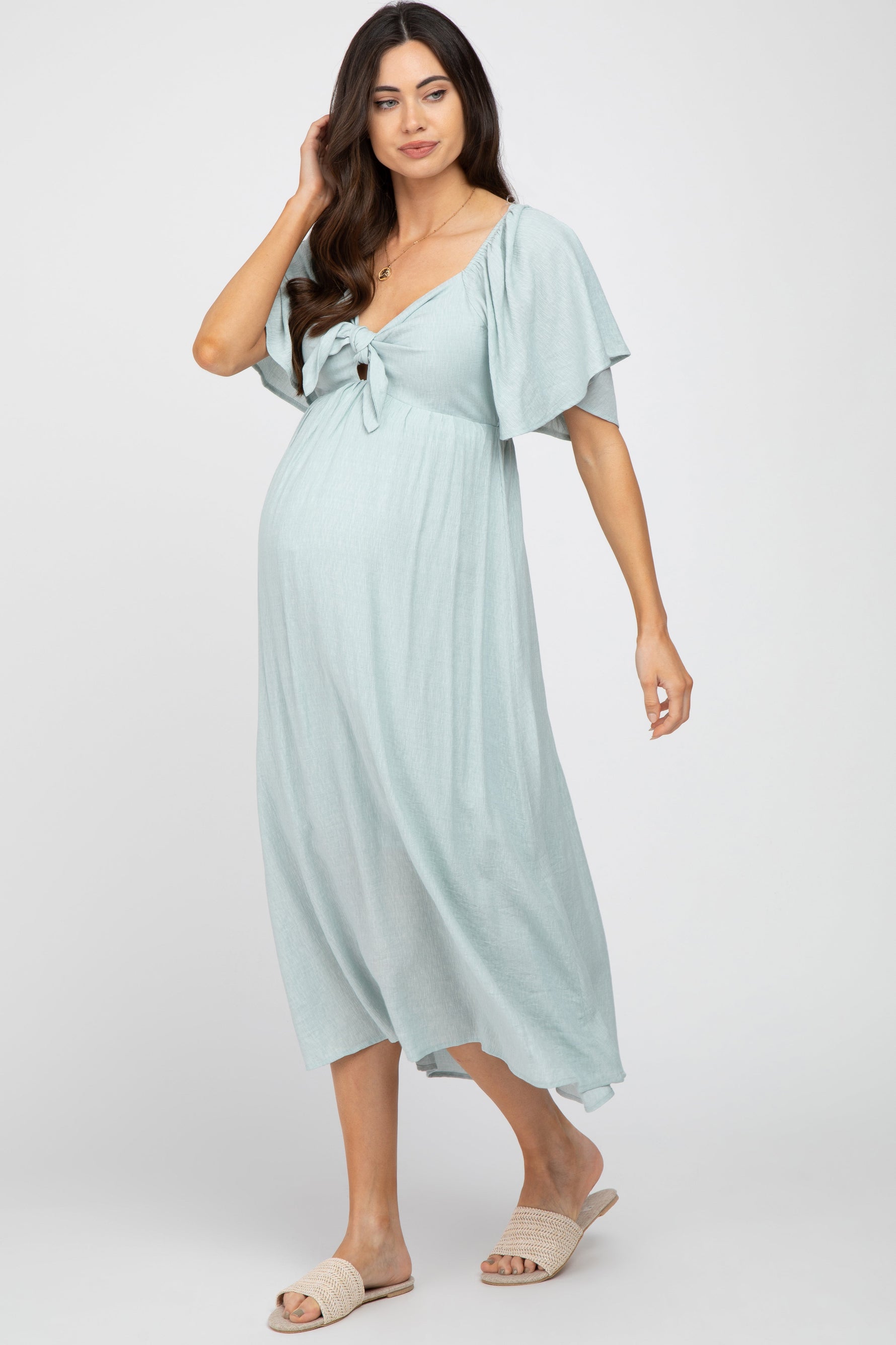 Model wearing a light blue ruffle sleeve maternity midi dress with a front tie detail, standing gracefully.