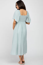Model wearing a light blue ruffle sleeve maternity midi dress with a front tie detail, standing gracefully.