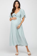 Model wearing a light blue ruffle sleeve maternity midi dress with a front tie detail, standing gracefully.
