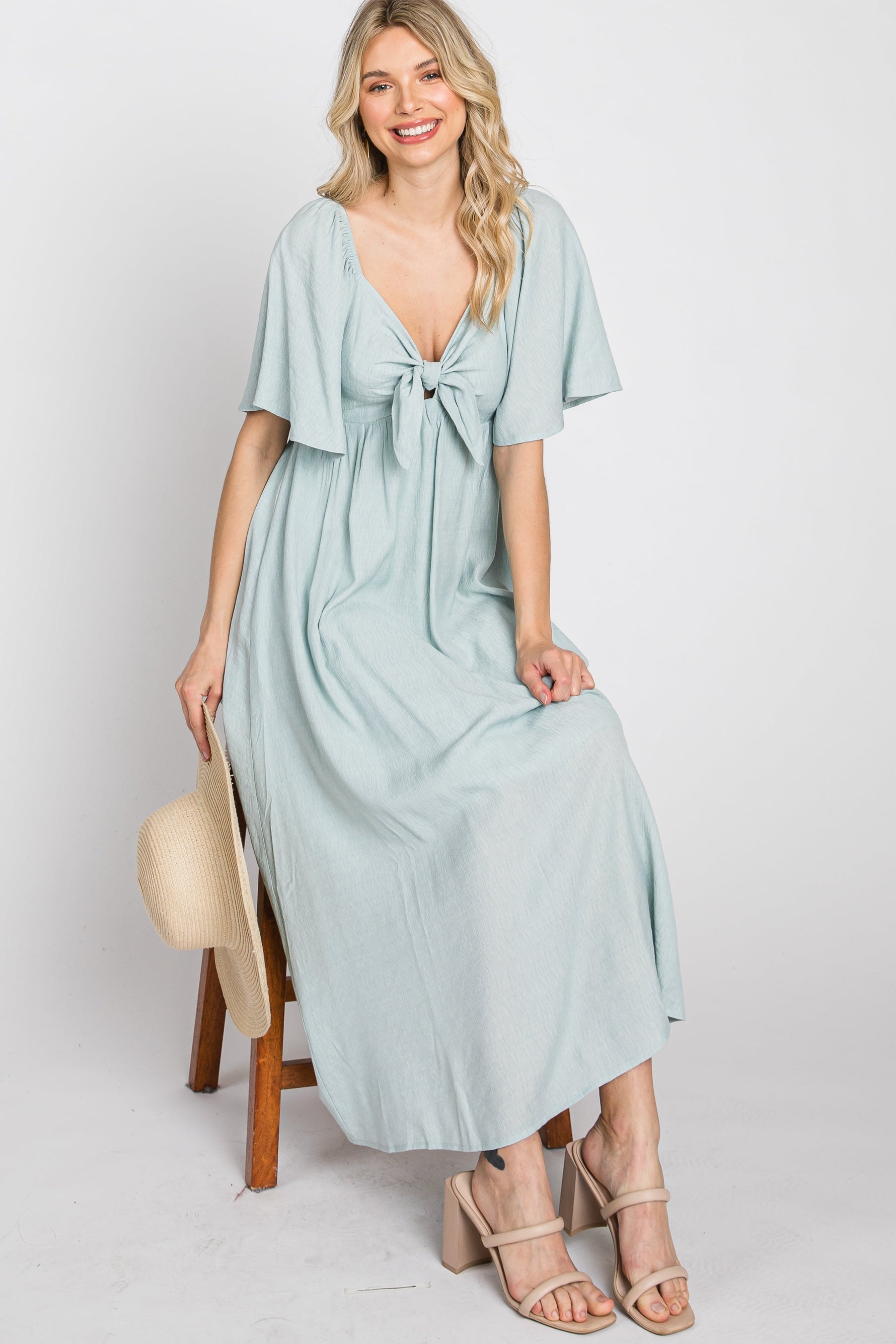 Model wearing a light blue ruffle sleeve maternity midi dress with a front tie detail, standing gracefully.