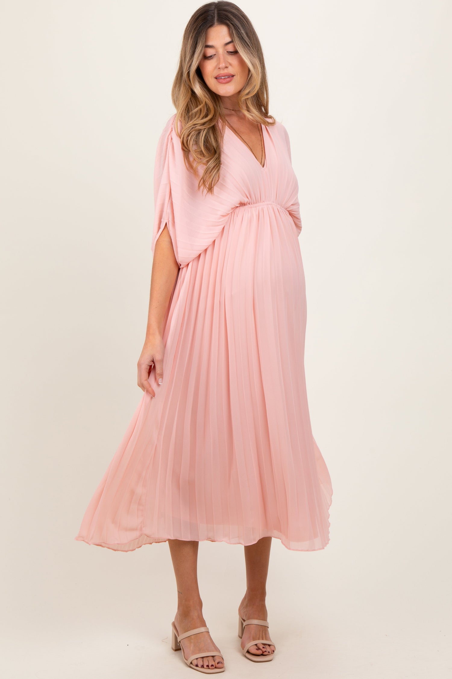 Light pink pleated V-neck maxi dress for maternity, worn by an expecting mother, standing gracefully.