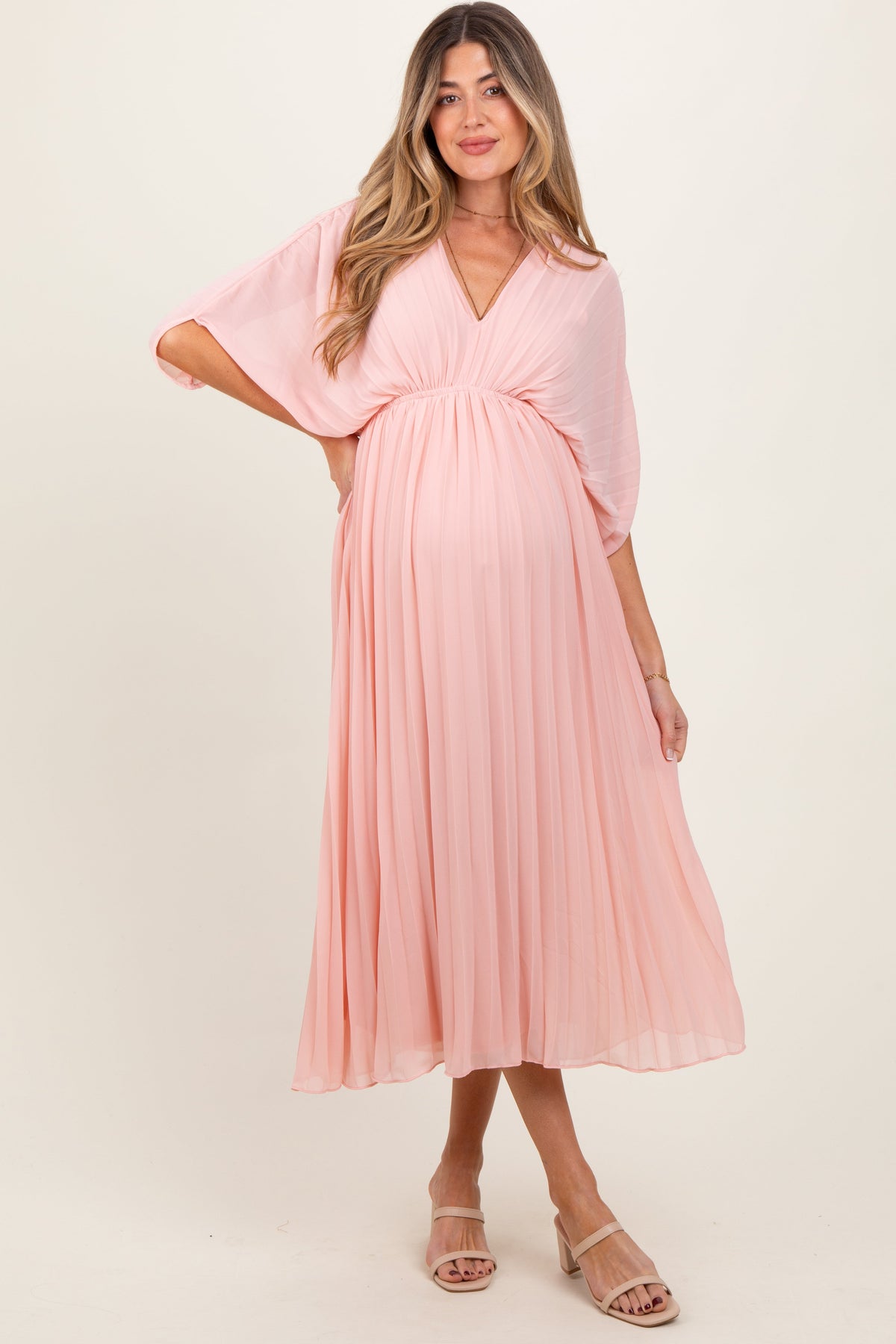 Light pink pleated V-neck maxi dress for maternity, worn by an expecting mother, standing gracefully.