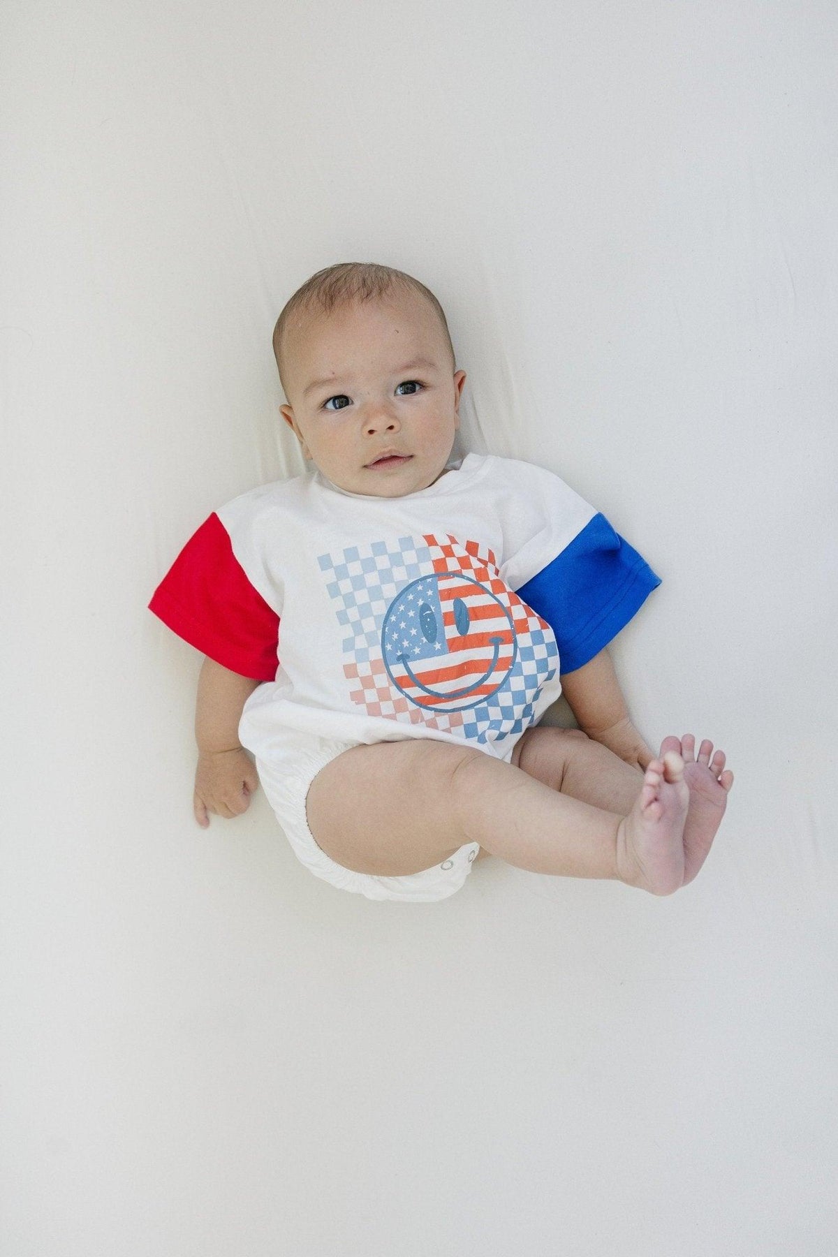 Little Joy Co. baby wearing a colorblock t-shirt romper with checkered flag and smile design
