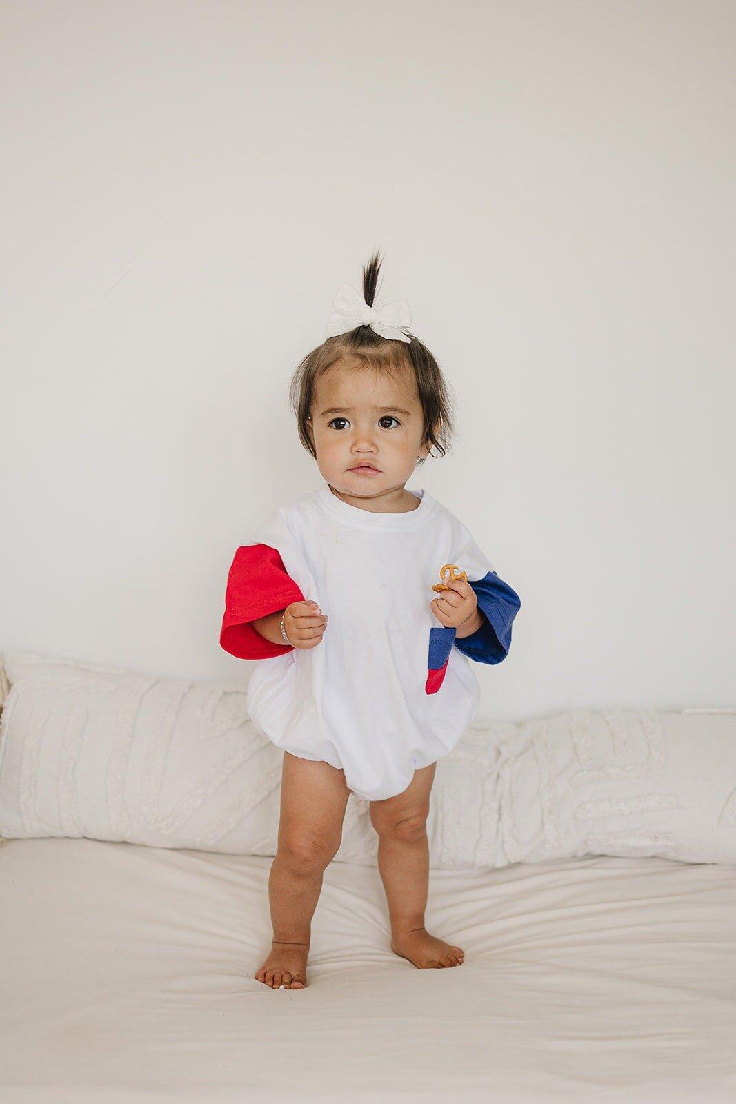 Baby wearing Little Joy Co. patriotic colorblock pocket t-shirt romper, smiling and playing.