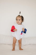 Baby wearing Little Joy Co. patriotic colorblock pocket t-shirt romper, smiling and playing.