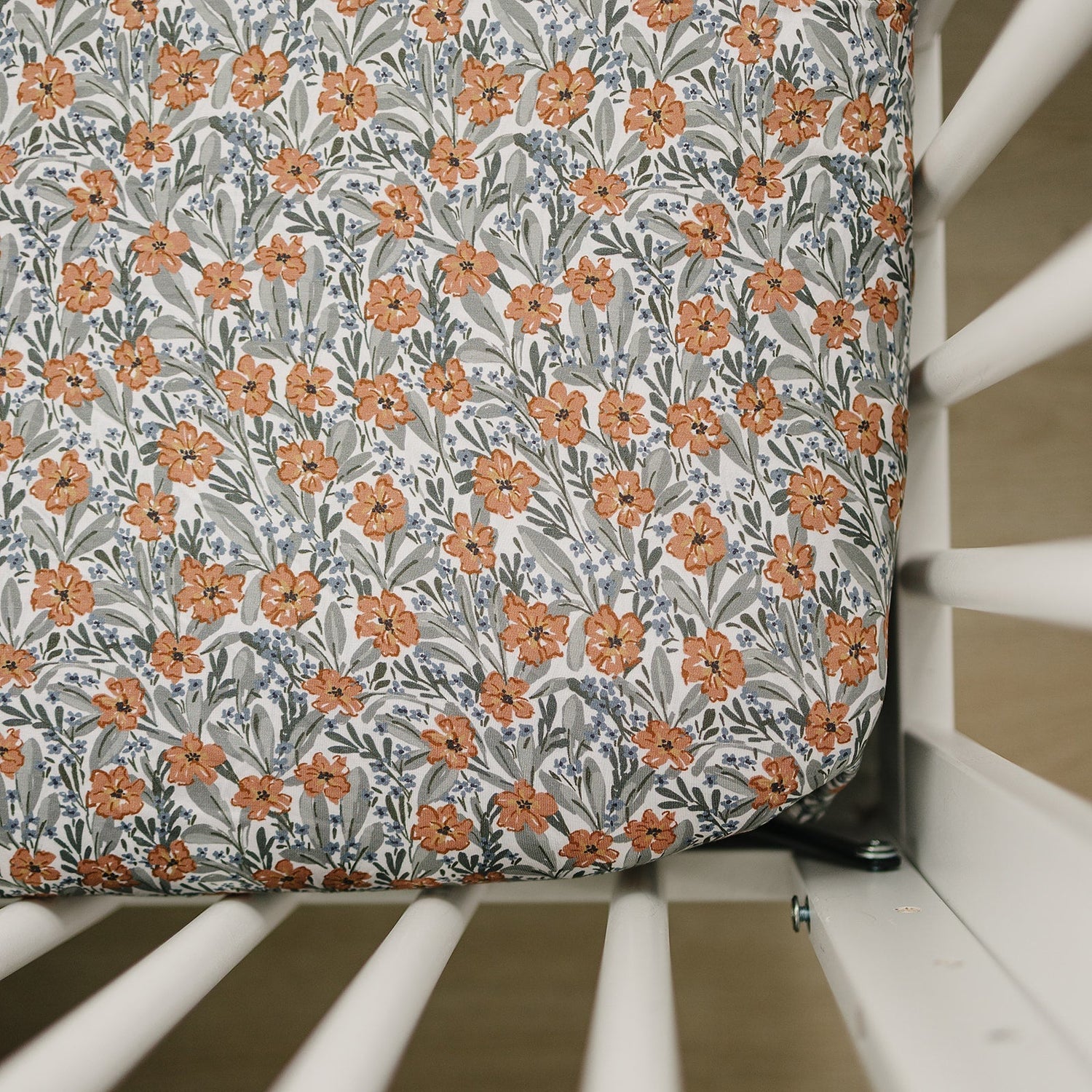 Crib sheet with a small floral meadow print in soft muted tones, fitted over a standard crib mattress.
