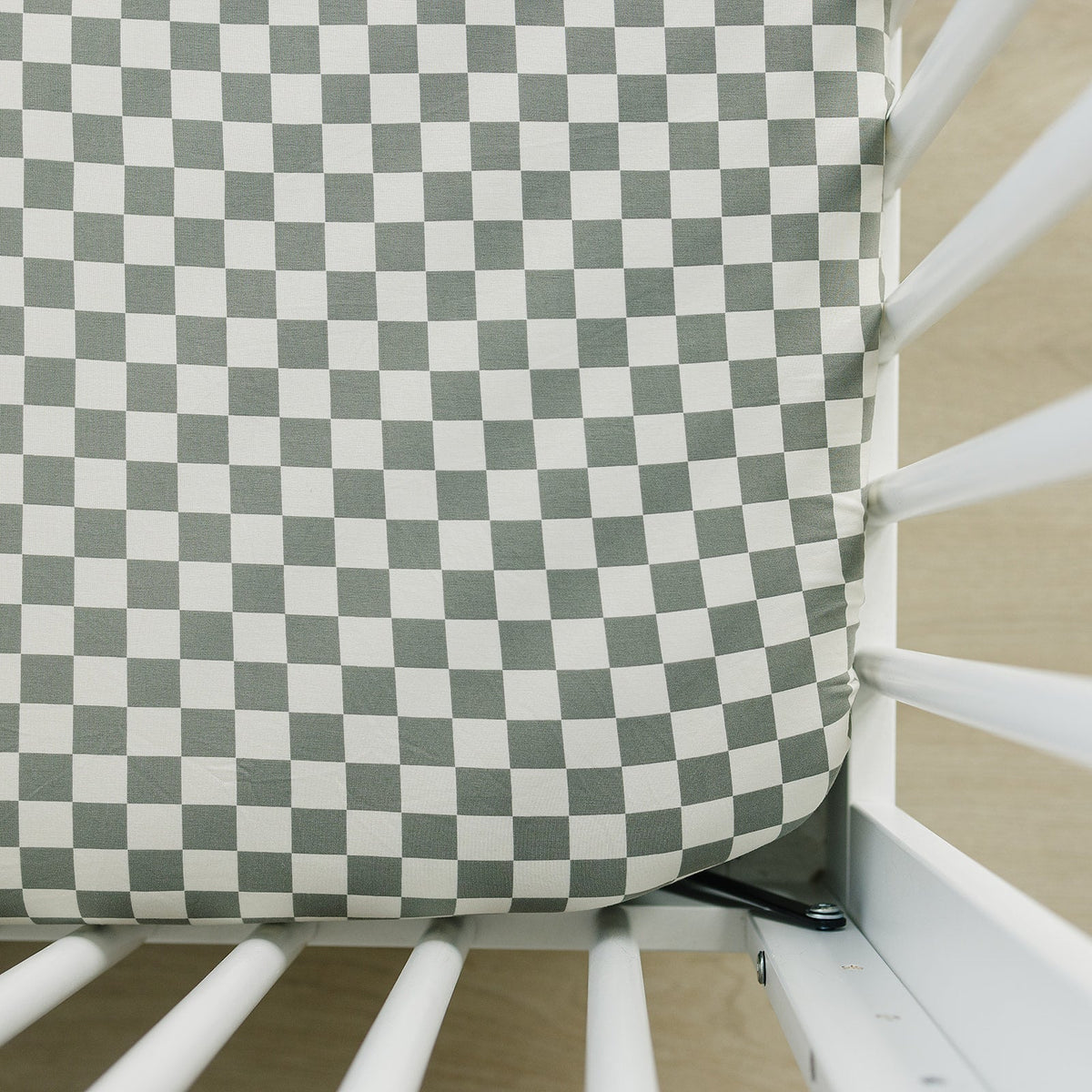 Light green and white checkered crib sheet fitted on a standard crib mattress