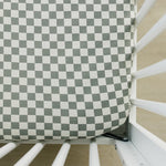 Light green and white checkered crib sheet fitted on a standard crib mattress