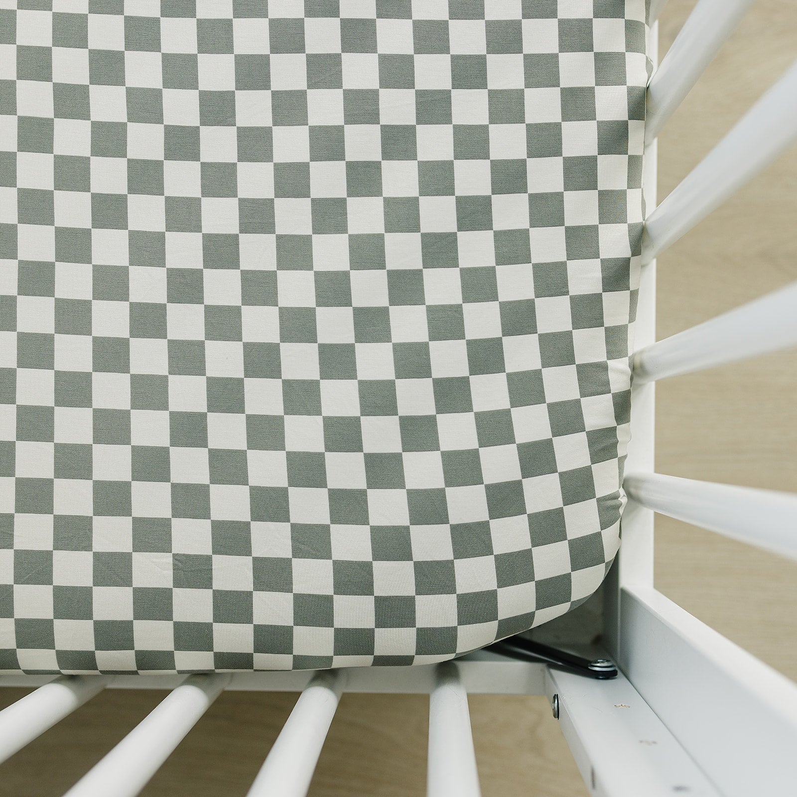 Light green and white checkered crib sheet fitted on a standard crib mattress