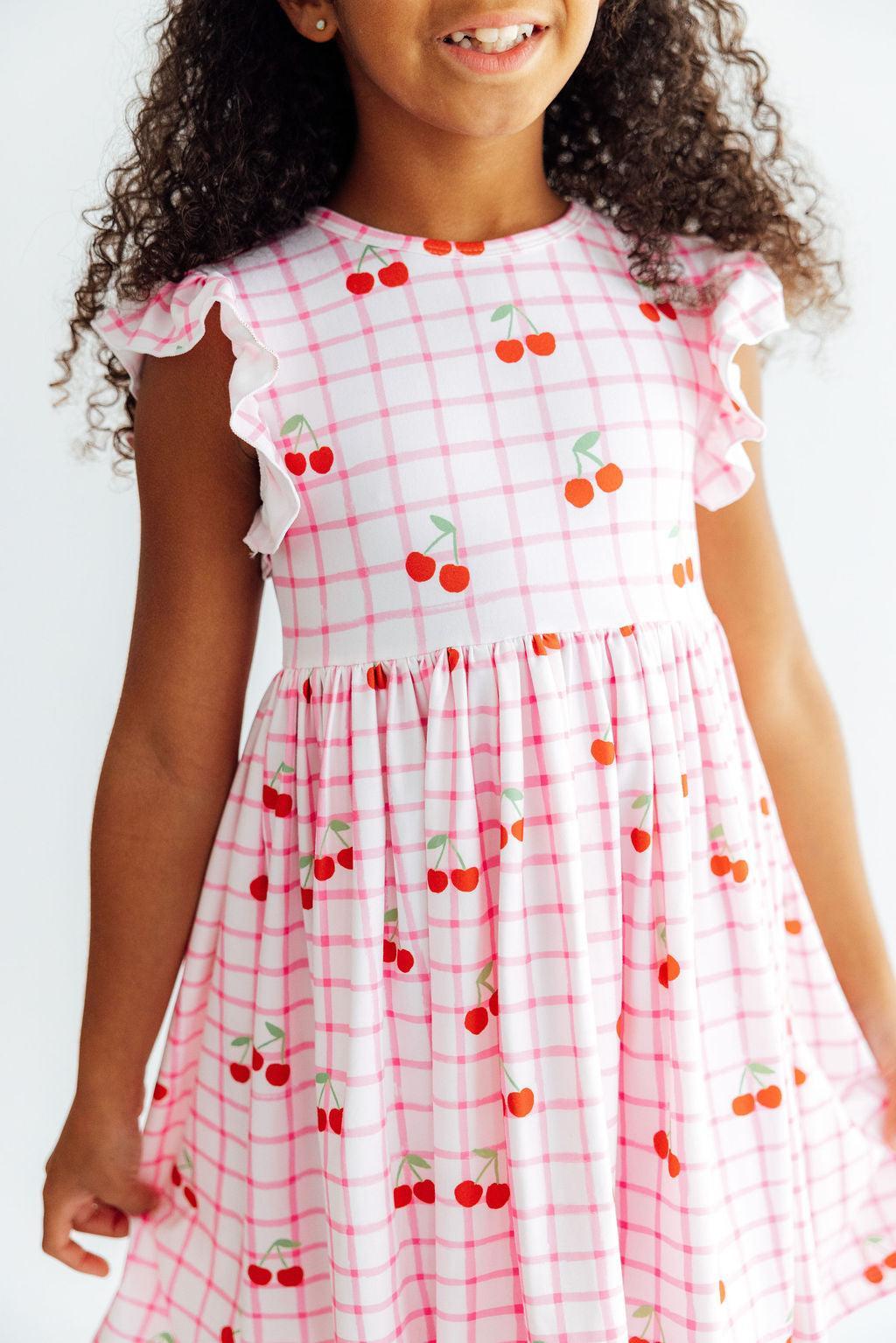 Twirl dress with flutter sleeves in a cherry print, showing scoop back and higher neckline