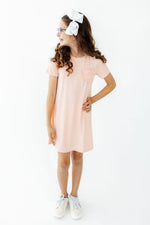 Peach t-shirt dress with short sleeves and a ruffle pocket on the front.
