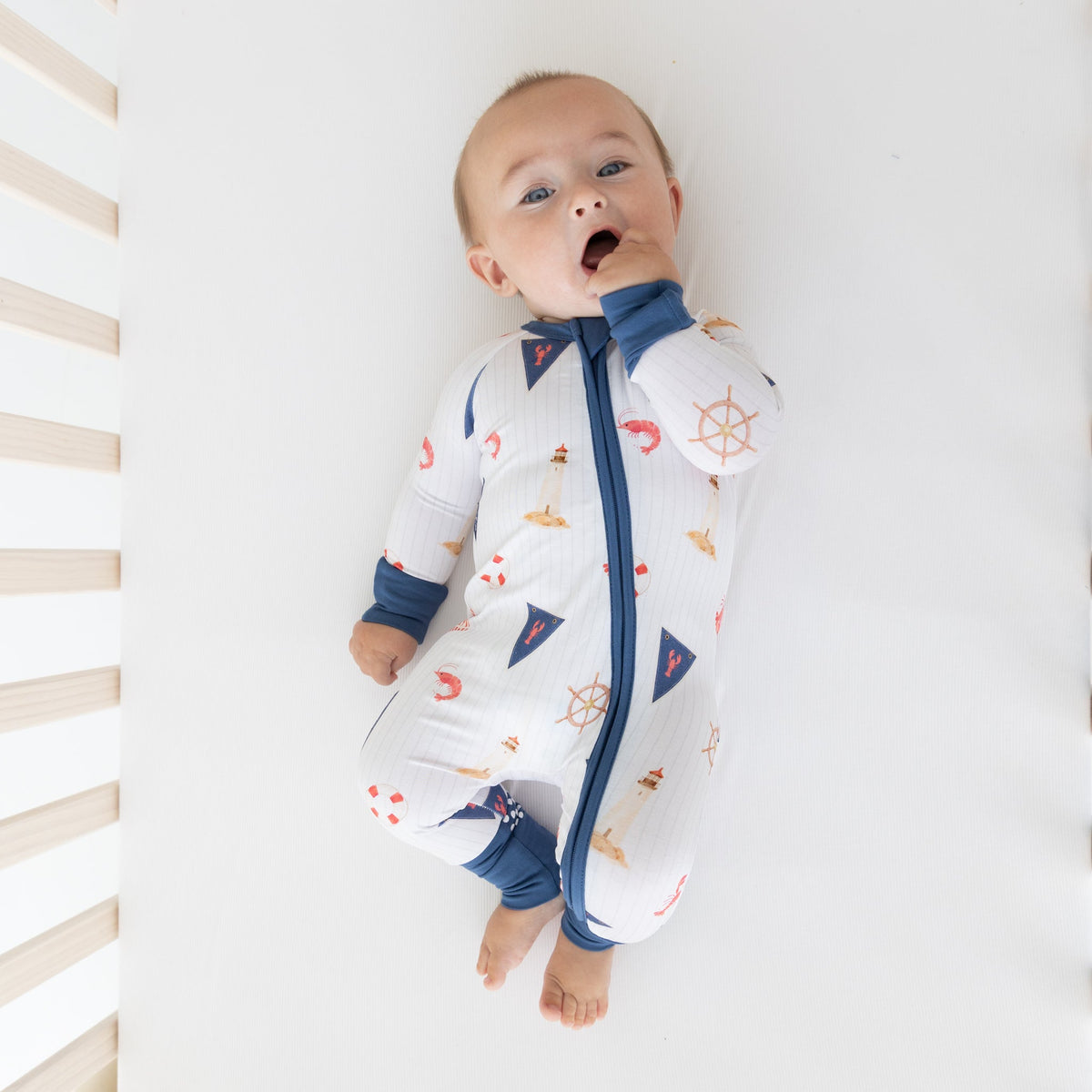 Baby zip-up pajamas in a nautical print with sailboats, lighthouses, ship wheels, and lobster flags.