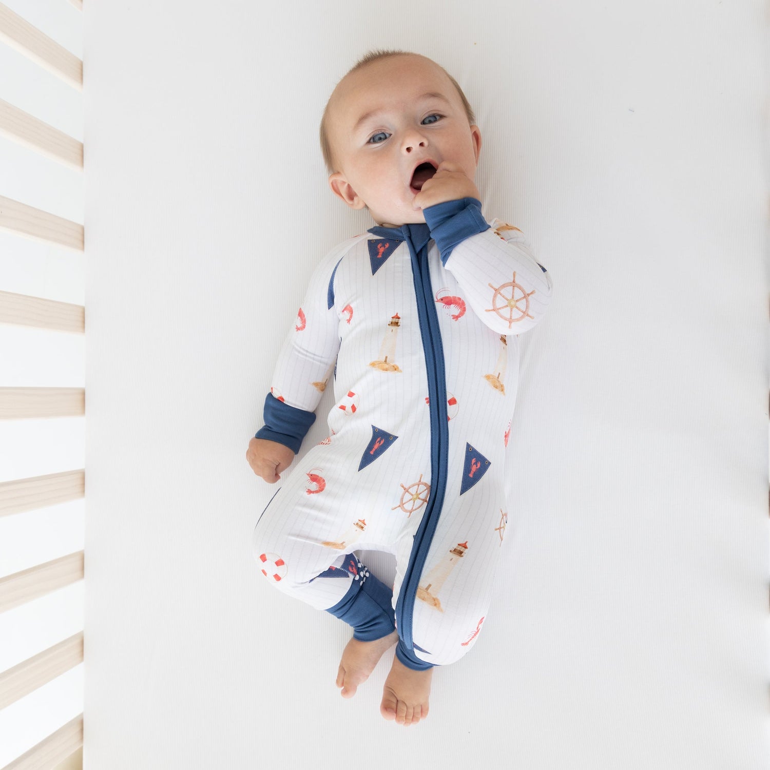 Baby zip-up pajamas in a nautical print with sailboats, lighthouses, ship wheels, and lobster flags.