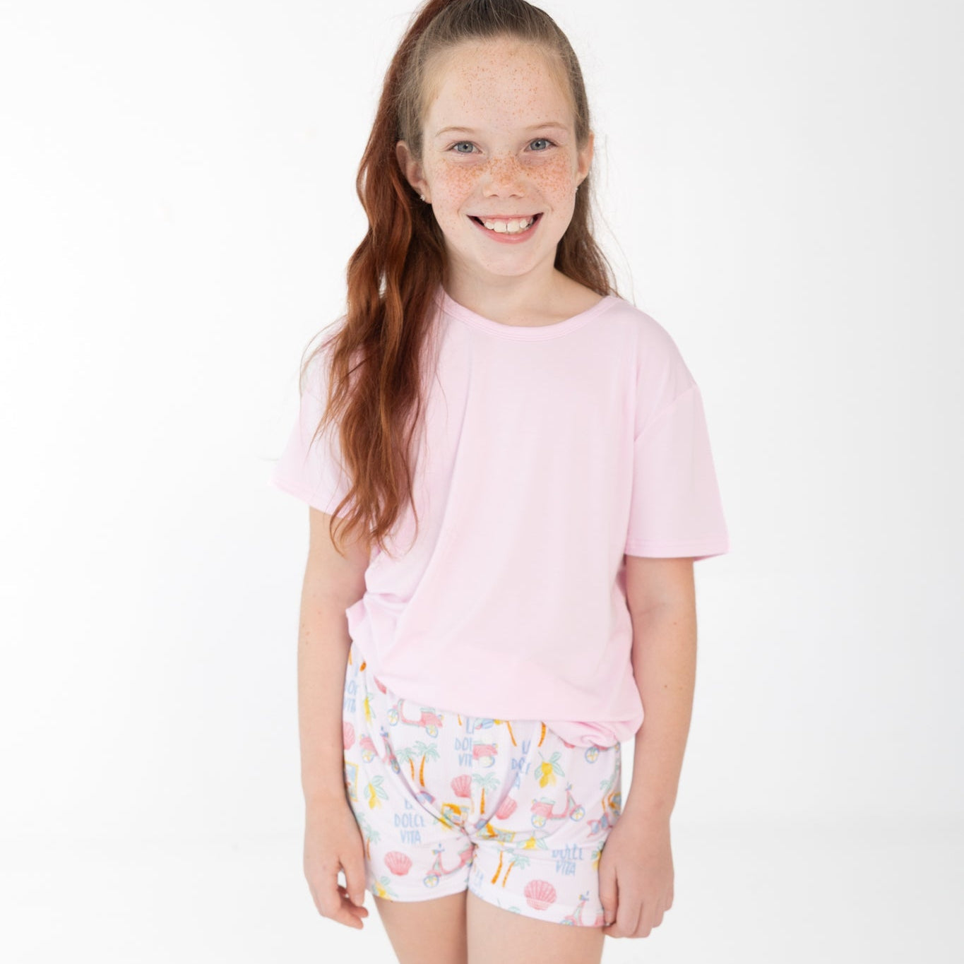 Girls shorts set with solid pink short-sleeve top and printed shorts with pink scooters, lemons, palm trees, and seashells.
