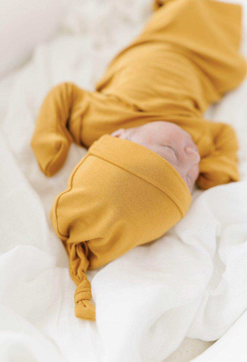Knot Hat in mustard color on a newborn baby, made of soft bamboo viscose and spandex.