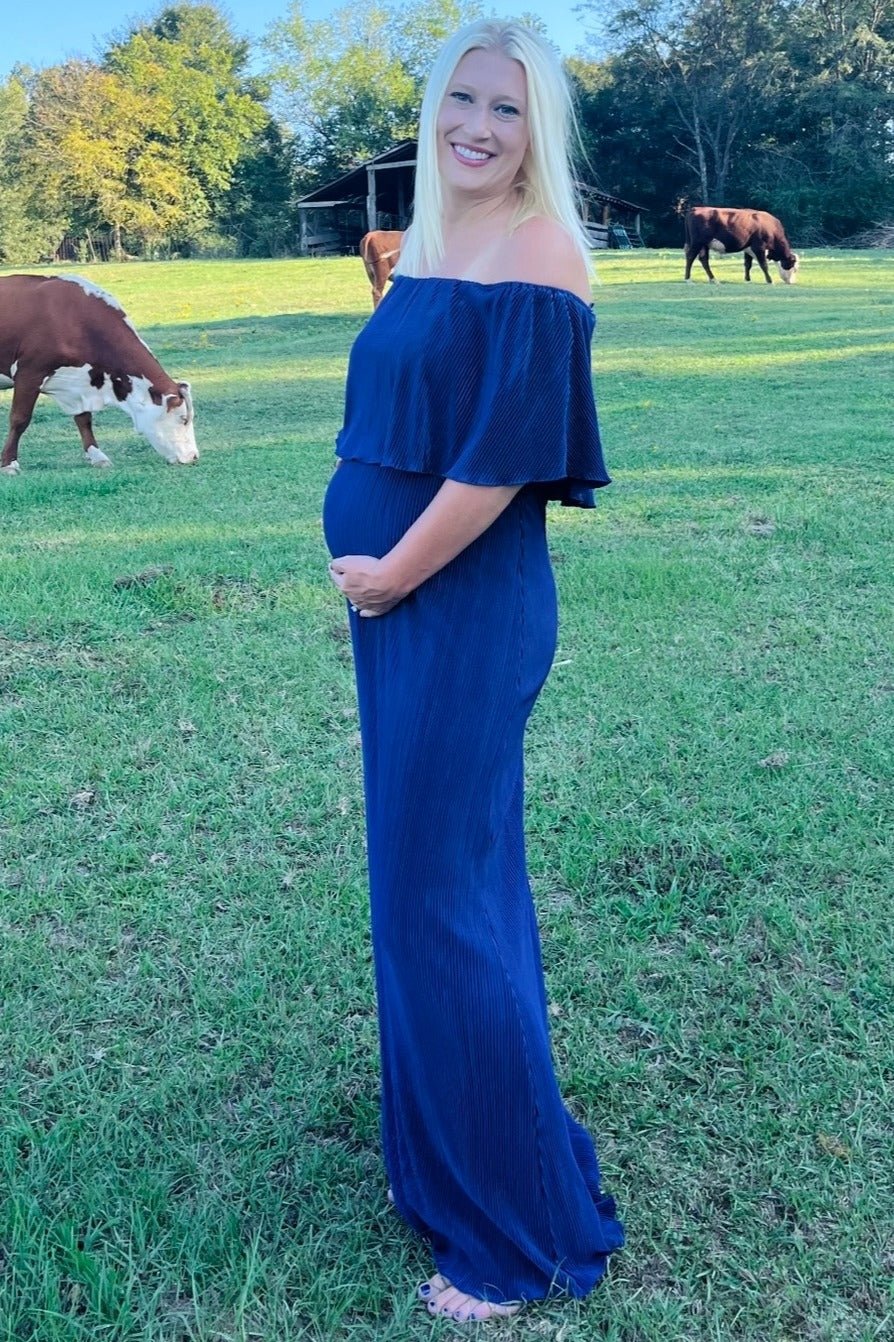 Model wearing a navy pleated ruffle off-shoulder maternity maxi dress by PinkBlush, smiling.