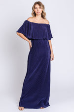 Model wearing a navy pleated ruffle off-shoulder maternity maxi dress by PinkBlush, smiling.