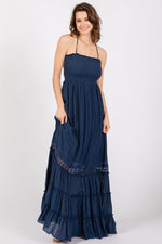 Model wearing a navy smocked open back maternity maxi dress, standing gracefully.