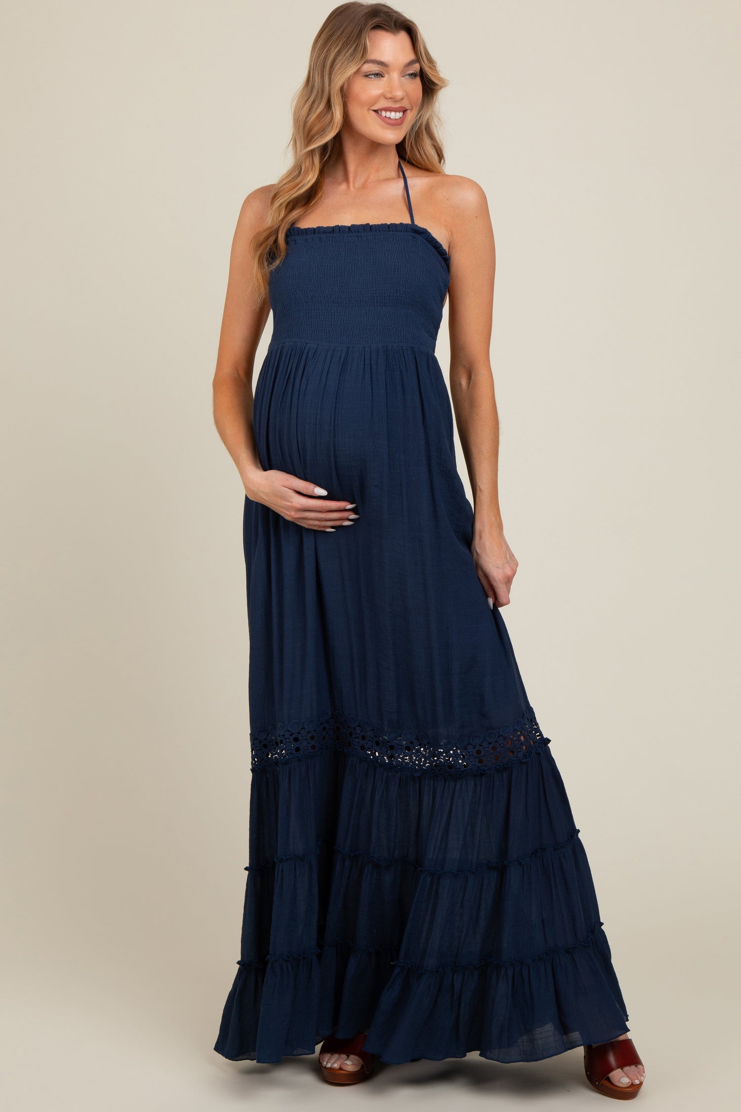 Model wearing a navy smocked open back maternity maxi dress, standing gracefully.