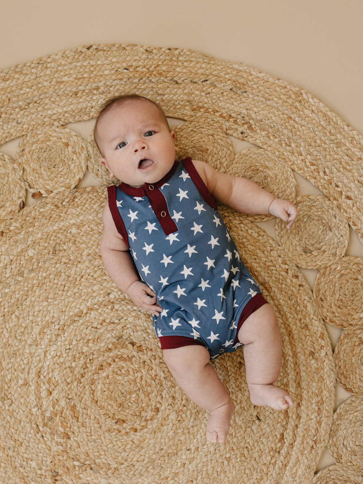 Little Joy Co. baby wearing a navy blue bamboo romper with white star print and Henley buttons