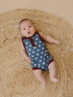Little Joy Co. baby wearing a navy blue bamboo romper with white star print and Henley buttons