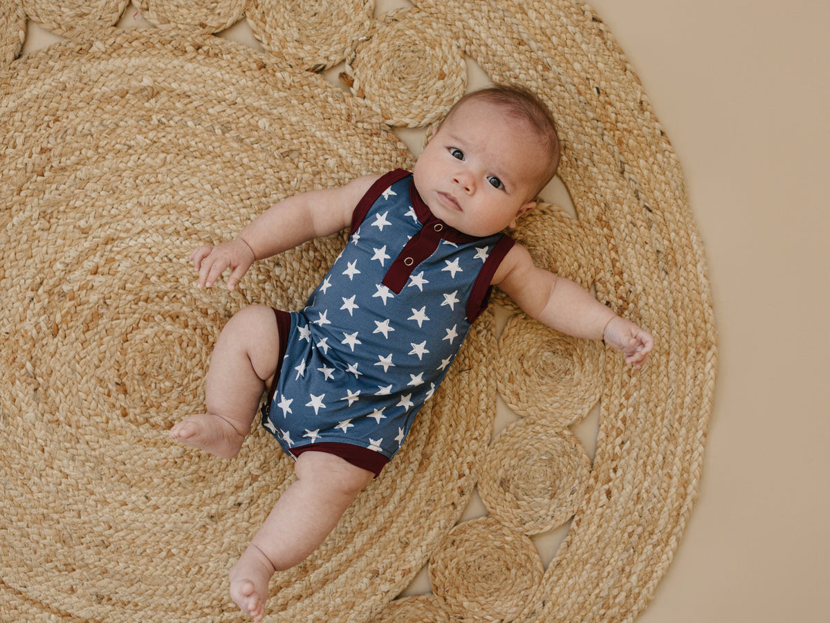 Little Joy Co. baby wearing a navy blue bamboo romper with white star print and Henley buttons