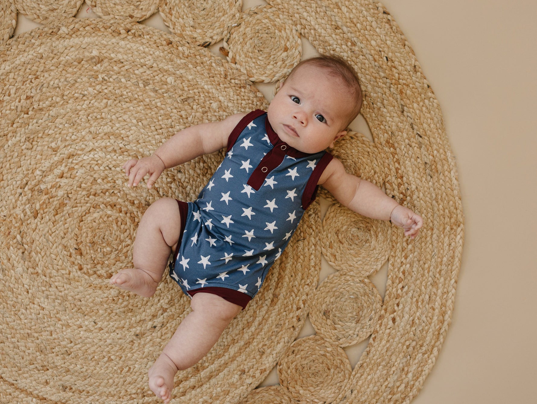 Little Joy Co. baby wearing a navy blue bamboo romper with white star print and Henley buttons