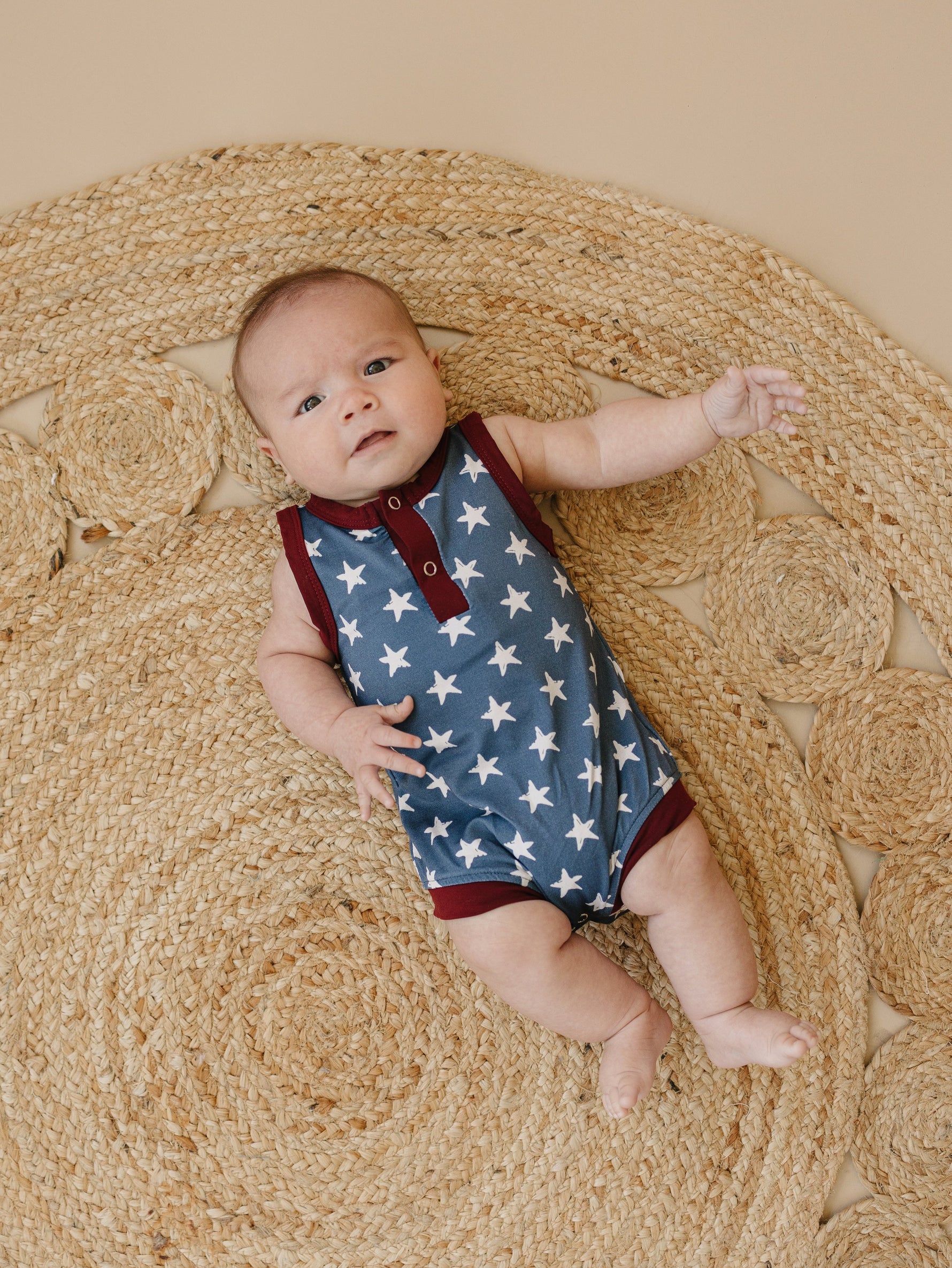 Little Joy Co. baby wearing a navy blue bamboo romper with white star print and Henley buttons