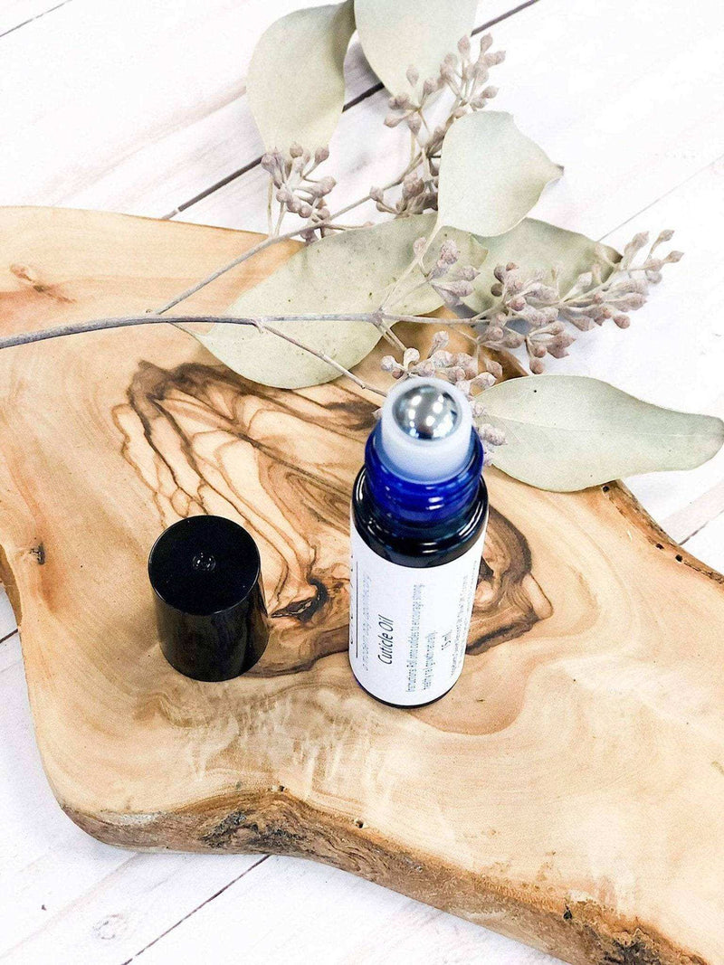 Organic cuticle oil bottle on wooden surface with dried flowers.