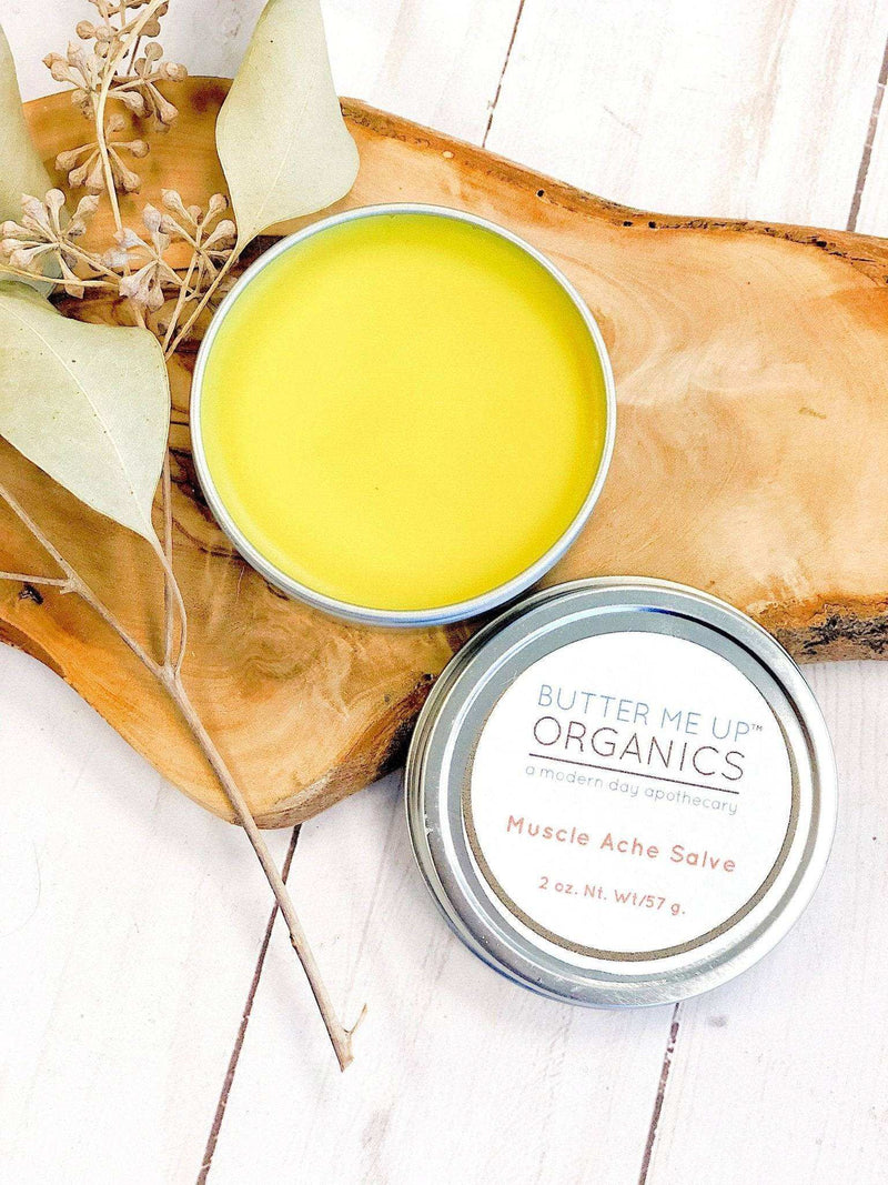 Organic Muscle Salve in a tin container with herbal ingredients on a wooden surface.