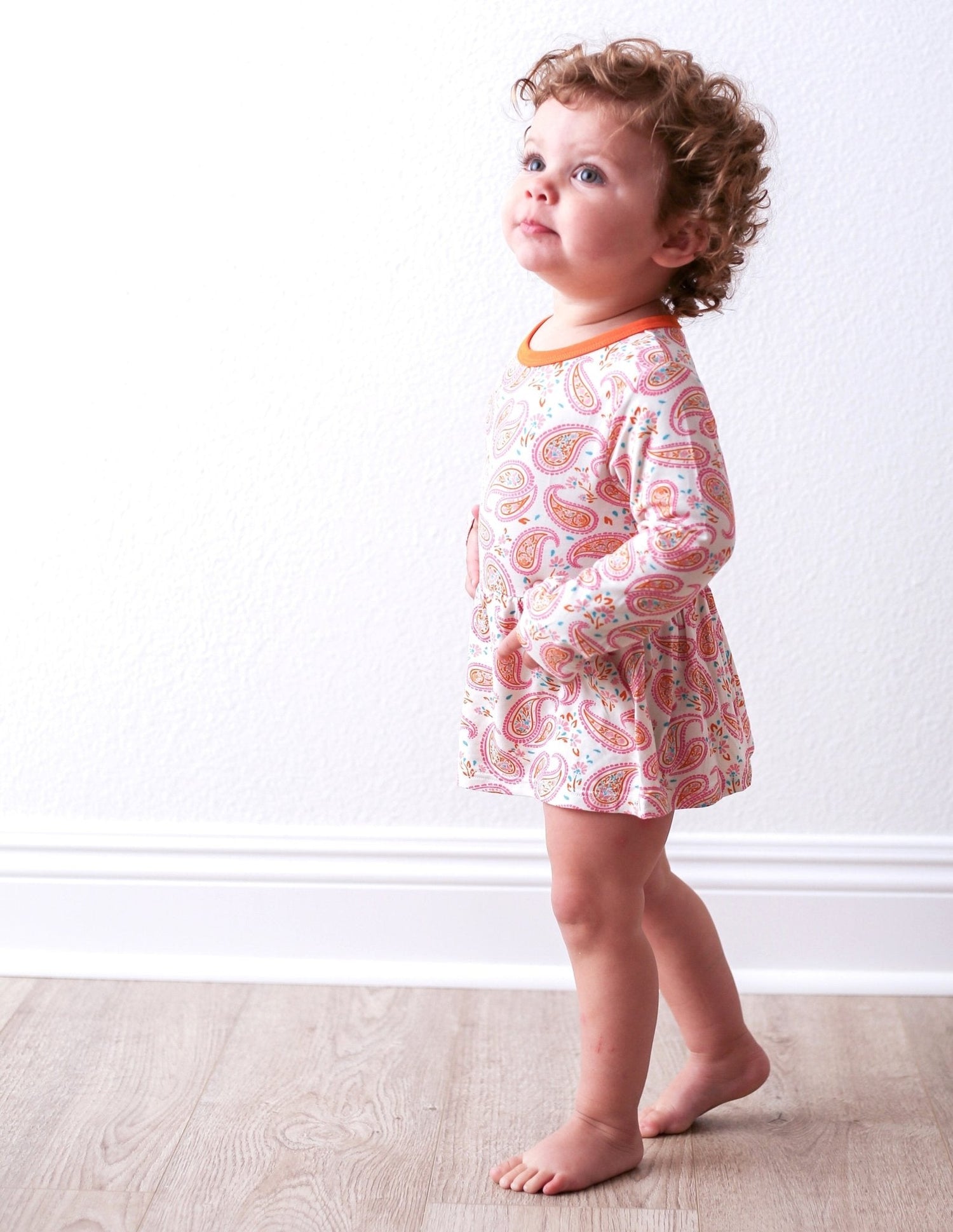 Paisley long-sleeve bodysuit dress in pink on a child model, with snap closure at the inseam.