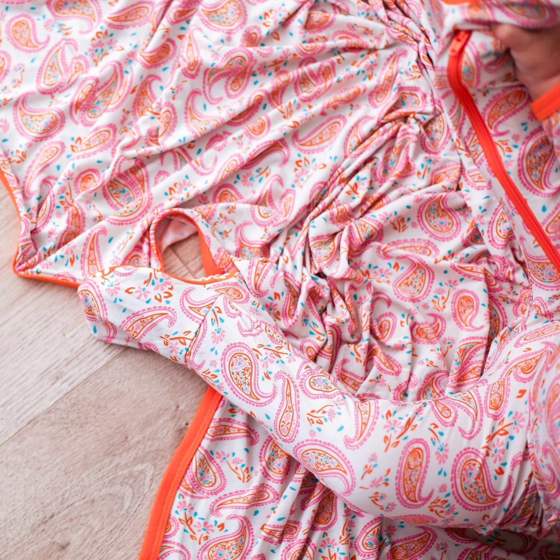 Paisley print swaddle blanket in pink and orange, spread out flat to show the pattern.