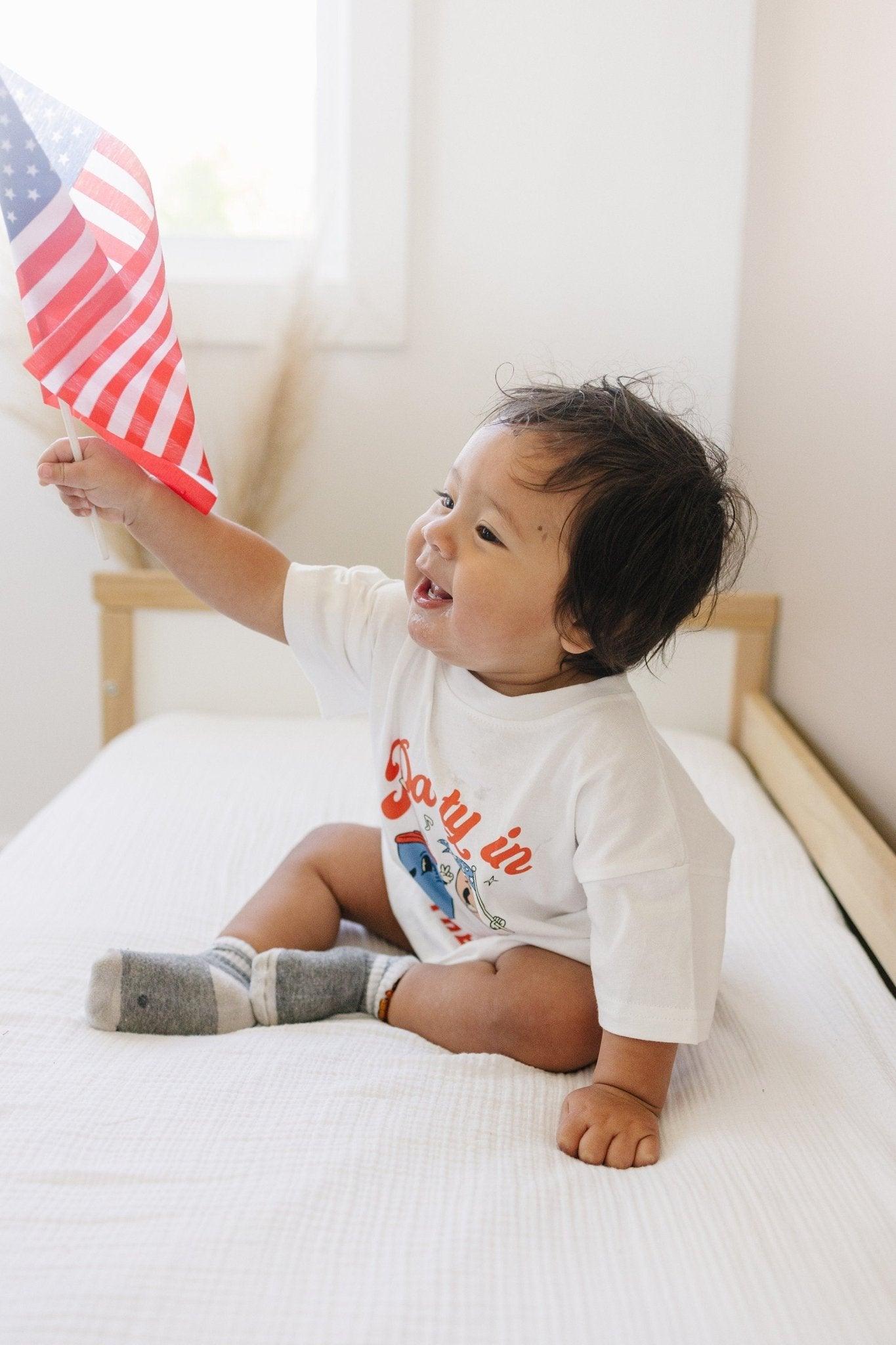 Little Joy Co. organic baby t-shirt romper with 'Party in the USA' graphic, front view