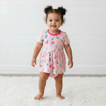 Short sleeve baby bodysuit dress with a petal and bug print and a flared skirt over a snap-bottom bodysuit