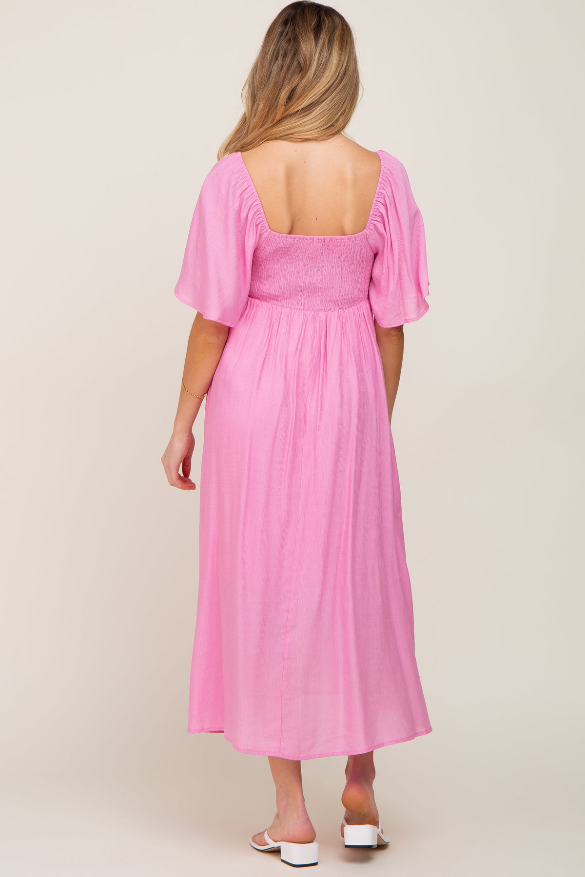 Pink maternity midi dress with ruffle sleeves and a front tie detail, worn by a pregnant woman.