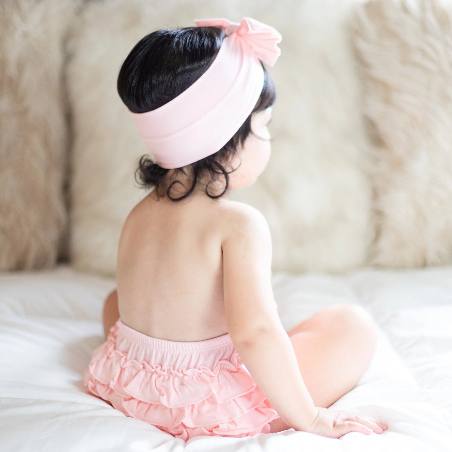 Baby wearing a rose-pink ruffle bloomer with back ruffles and a matching stretchy headband.