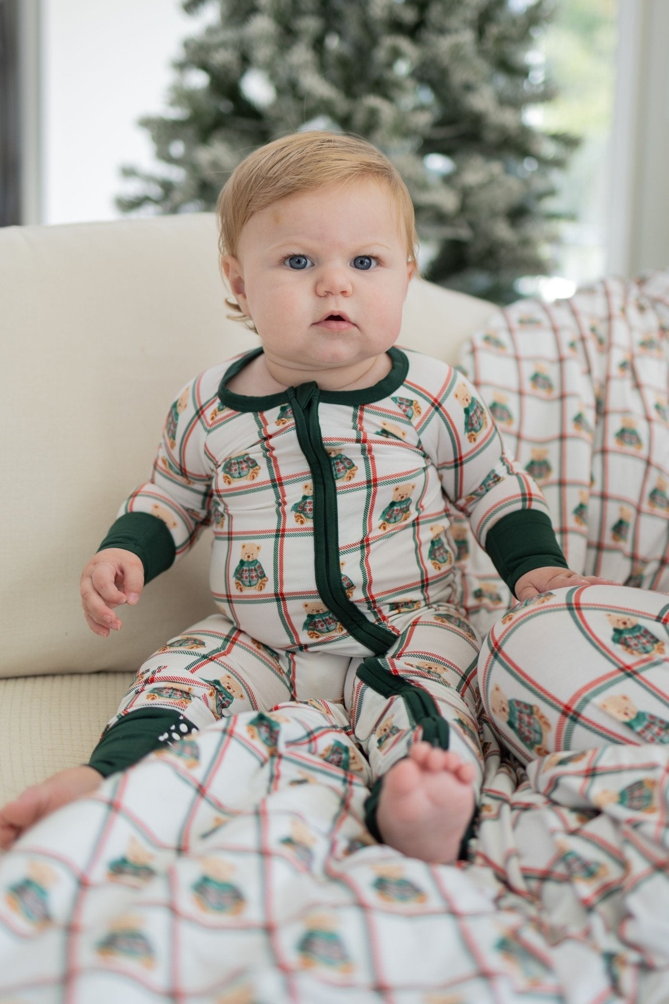 Baby bamboo footed romper with teddy bears in green sweaters on a plaid Christmas background and fold-over feet